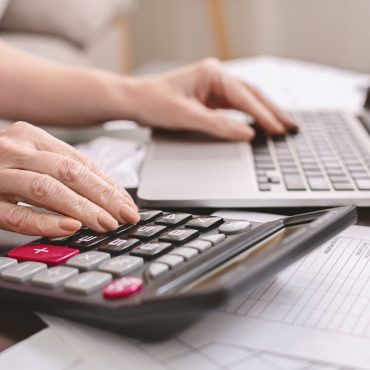 senior woman with calculator counting dollar money at home