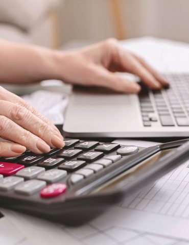 senior woman with calculator counting dollar money at home